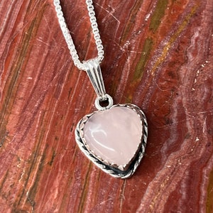 Puede incluir: Un collar de cadena de plata con un colgante en forma de coraz&oacute;n rosa. El colgante tiene un borde plateado con un dise&ntilde;o delicado.