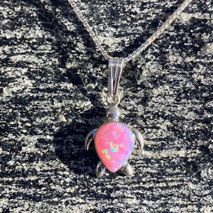 May include: A silver chain necklace with a pink opal turtle pendant. The turtle is made of sterling silver and has a detailed design.
