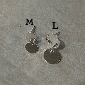 May include: Two pairs of silver earrings with a hammered texture. The earrings are labeled "M" and "L" to indicate size.