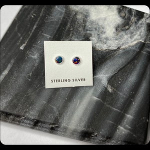 May include: A pair of sterling silver stud earrings with round, iridescent opal stones. The earrings are displayed on a white card with the text "Sterling Silver".