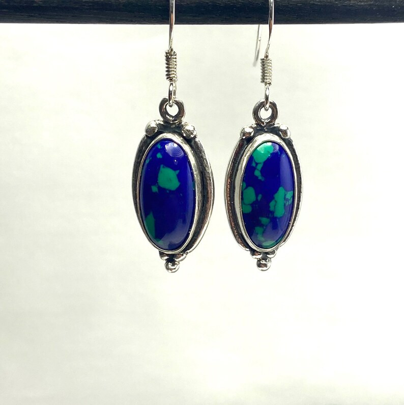 May include: A pair of silver dangle earrings with oval-shaped blue and green gemstone accents.