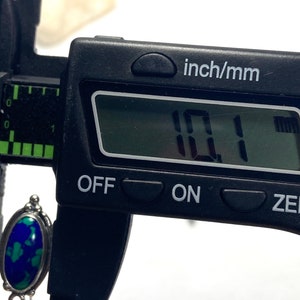 May include: Close-up of a digital caliper measuring a turquoise and silver pendant. The caliper reads 10.1 mm.