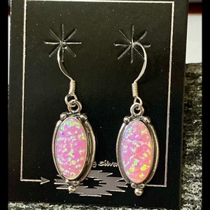 K&ouml;nnte beinhalten: Ein Paar silberne Ohrringe mit rosafarbenen Opal-Steinen. Die Ohrringe haben ein schlichtes Design mit einem kleinen ovalen Stein.