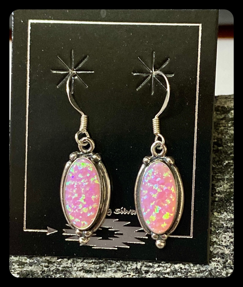 K&ouml;nnte beinhalten: Ein Paar silberne Ohrringe mit rosafarbenen Opal-Steinen. Die Ohrringe haben ein schlichtes Design mit einem kleinen ovalen Stein.