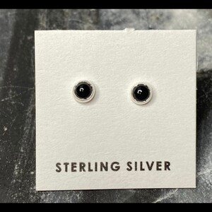 May include: A pair of sterling silver stud earrings with black onyx stones. The earrings are displayed on a white card with the text "STERLING SILVER" printed on it.