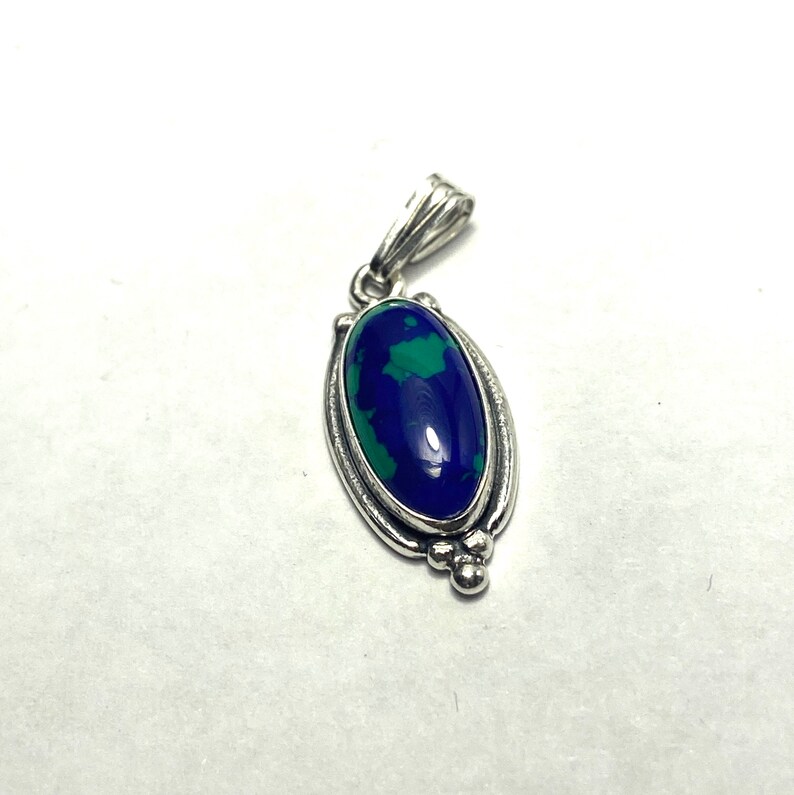 May include: A silver pendant featuring a blue and green oval gemstone set in a silver frame. The pendant has a bail for attaching to a chain.