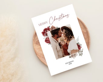 May include: A white Christmas card with a family photo, framed with burgundy floral accents. The words "MERRY Christmas" are written at the top, with "THE SMITHS 2023" at the bottom. The card is on a wooden plate.