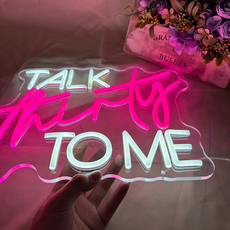 Może przedstawiać: R&oacute;żowy neonowy znak z tekstem "Talk Thirty To Me" w białej, falistej, chmurowatej ramce.