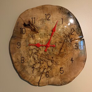 Peut inclure: Une horloge en bois avec une aiguille des heures rouge et une aiguille des minutes noire. Le cadran de l'horloge est fait d'une tranche d'arbre avec un motif de grain de bois naturel. Les chiffres de 1 à 12 sont imprimés sur le cadran de l'horloge.
