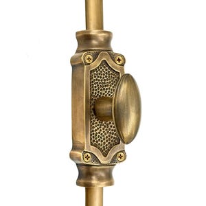 Puede incluir: Un cerrojo de puerta vertical de latón antiguo con un asa ovalada y un panel central texturizado. El cerrojo está montado sobre una varilla de latón y asegurado con tornillos pequeños. La ferretería tiene una estética vintage.