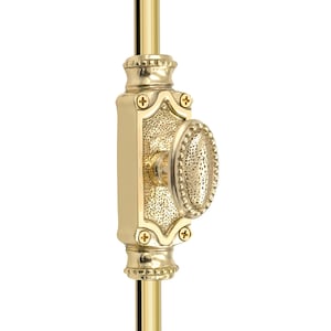 Może przedstawiać: Zbliżenie złotego uchwytu do okna. Uchwyt ma owalny uchwyt o teksturowanej powierzchni i jest zamontowany na pionowym pręcie. Projekt zawiera dekoracyjne detale i małe śruby.