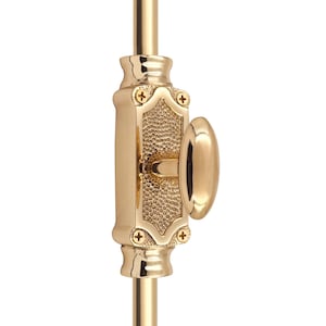 Puede incluir: Primer plano de un cerrojo de puerta de latón pulido. El cerrojo presenta un tirador ovalado y una placa rectangular texturizada con detalles decorativos. El cerrojo está montado sobre una varilla vertical.