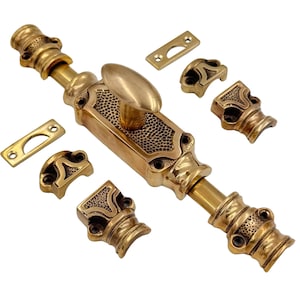 Op de afbeelding: Een set antieke messing deurbeslag, inclusief een lange grendel, een handvat en verschillende decoratieve montageonderdelen. De hardware heeft een verouderd, sierlijk ontwerp met een warme, gouden tint.