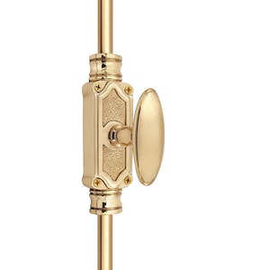 Könnte beinhalten: Ein polierter Fensterriegel aus Messing mit ovalem Griff. Das Schloss hat einen rechteckigen Körper mit dekorativen Details und ist an einer vertikalen Stange befestigt. Die Hardware hat eine helle Goldfarbe.
