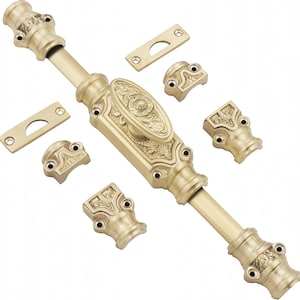Könnte beinhalten: Ein Fensterriegel-Set aus Messing mit einem zentralen Schiebemechanismus mit ovalem Griff, verzierten Blumendetails, zwei rechteckigen Schließblechen und vier Montagehalterungen, alles in einem polierten, metallischen Goldton.