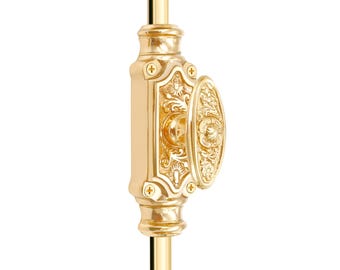 May include: A gold-colored, ornate window sash lock. The lock features an oval handle and a rectangular base, both with detailed floral and scrollwork designs. The hardware is mounted on a gold rod.