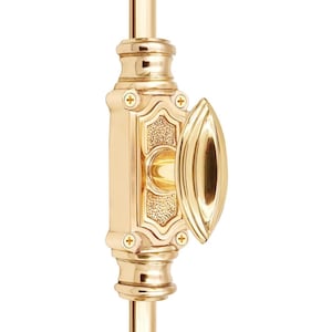 Puede incluir: Primer plano de un pestillo de ventana de latón pulido. La cerradura presenta un diseño ornamentado con un tirador decorativo y está montada sobre una varilla vertical. La ferretería es de color dorado brillante.