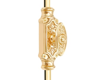 May include: A gold-colored, ornate window sash lock. The lock features an oval handle and a rectangular base, both with detailed floral and scrollwork designs. The hardware is mounted on a gold rod.