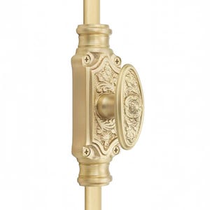May include: A brass window sash lock featuring an oval-shaped knob and a rectangular base plate with intricate embossed floral scrollwork. The hardware is secured with four visible screws and is mounted on a vertical brass rod component.