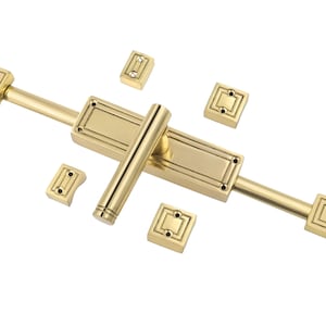 Op de afbeelding: Een gouden deurgrendel met een decoratief ontwerp. De grendel heeft een lange hendel en twee vierkante platen aan elk uiteinde.