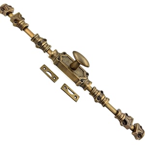 Op de afbeelding: Een antieke messingkleurige deursluiting met decoratieve details. De grendel heeft een ovale handgreep en twee bijpassende sluitplaten. De hardware is ontworpen voor een deur of kast en heeft een verouderde, vintage uitstraling.