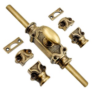 May include: Antique brass finish door bolt with decorative detailing. Includes the main bolt, strike plate, and several mounting pieces. The bolt features an oval handle and a textured center section. Hardware for doors and furniture.