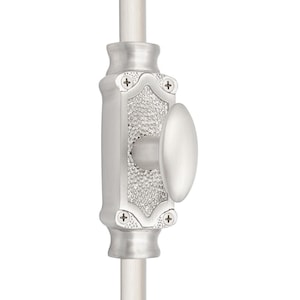 Op de afbeelding: Een zilverkleurige deursluiting met een ovale handgreep. De grendel heeft een getextureerd midden en is versierd met decoratieve elementen en kruisvormige accenten. Het is gemonteerd op een witte staaf.