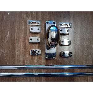 Op de afbeelding: Een verzameling gepolijste chromen hardware-componenten, waaronder een centrale ovale handgreep, verschillende rechthoekige montageplaten en twee lange, gebogen staven. De onderdelen zijn gerangschikt op een houten oppervlak.