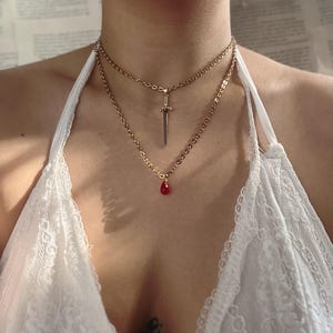 May include: A gold chain necklace with a sword pendant and a red teardrop pendant.