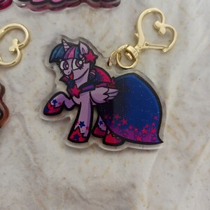 May include: A purple and blue cartoon pony with a pink and blue dress and a gold star charm keychain.