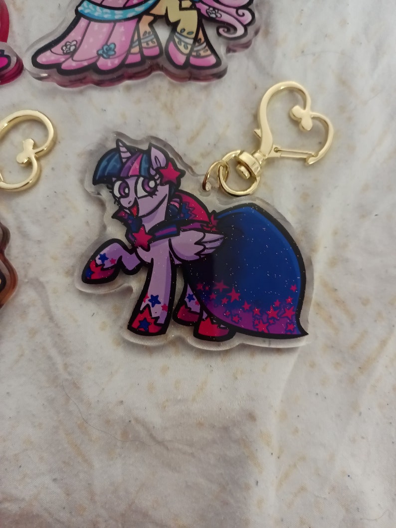 May include: A purple and blue cartoon pony with a pink and blue dress and a gold star charm keychain.