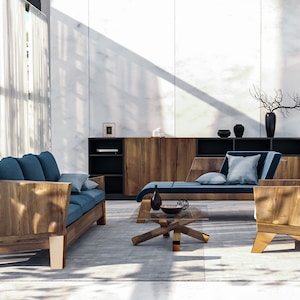Op de afbeelding: Een moderne woonkamerset met een houten bank, een chaise longue en een fauteuil met blauwe kussens. Een houten kast en een glazen salontafel maken het geheel compleet. De kamer is gedecoreerd met vazen en een decoratieve tak.
