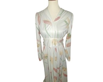 May include: A long-sleeved white dress with a floral print featuring pink, yellow, and green flowers. The dress has a V-neckline and a fitted bodice. The skirt is full and flowing.