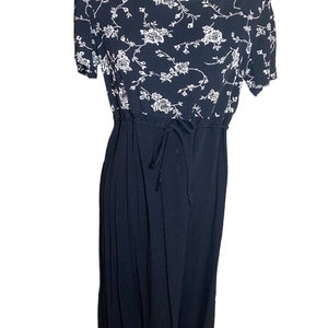 May include: A navy blue dress with a white floral pattern on the bodice. The dress has short sleeves, a drawstring waist, and a pleated skirt. Buttons run down the front of the skirt.