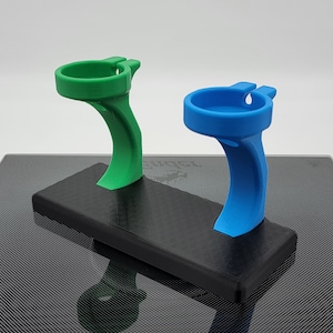 May include: A black stand with two holders for small objects. One holder is green and the other is blue.