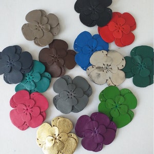 Könnte beinhalten: Zwölf Lederblumen-Verzierungen in verschiedenen Farben, darunter Schwarz, Grau, Braun, Teal, Rot, Blau, Gold, Grün, Lila und Beige.