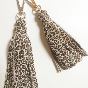 Puede incluir: Dos llaveros de estampado de leopardo con anillas de plata y oro. Las borlas están hechas de una tela suave, de color marrón claro con estampado de leopardo negro.