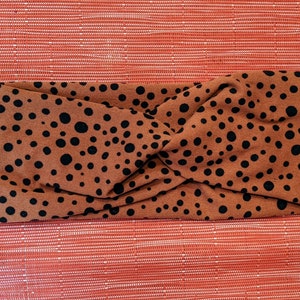 May include: A brown headband with a black polka dot pattern. The headband is twisted and folded.