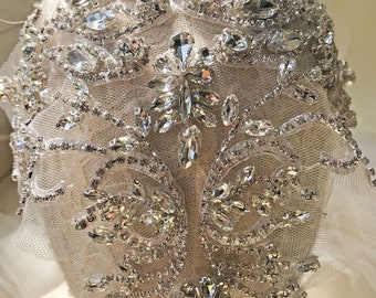 Puede incluir: Un diseño delicado e intrincado de pedrería y cristales, dispuestos en un patrón floral, sobre un fondo de tela blanca. El diseño es perfecto para agregar un toque de brillo a cualquier proyecto.