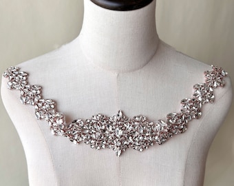 May include: A rose gold bridal sash with clear crystal embellishments. The sash is designed to be worn around the waist or as a neckline embellishment.