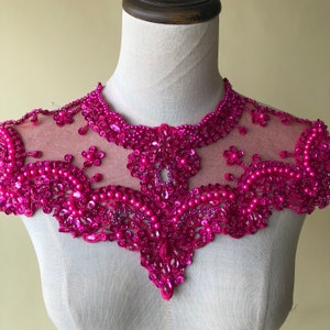 May include: A pink beaded and sequined collar necklace with a sheer mesh backing. The collar is decorated with pink beads and sequins in a floral pattern.