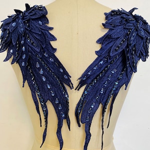 May include: A pair of navy blue fabric wings with blue sequins. The wings are designed to be sewn onto a garment.