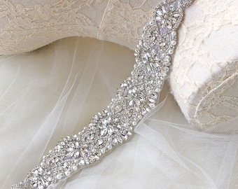 May include: A silver beaded bridal belt with a delicate pearl design. The belt is made of rhinestones and pearls and is perfect for adding a touch of sparkle to a wedding dress.