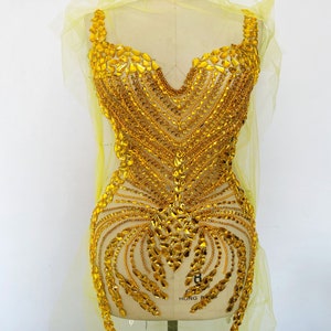 Peut inclure: Une applique de perles dorées avec un décolleté en V et un design en cascade. L'applique est sur un tissu en maille jaune.