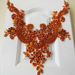 Può includere: Applique di perline arancioni con un motivo floreale. L'applique è realizzata con piccole perline rotonde e presenta un motivo delicato e intricato.