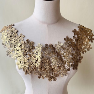 Może przedstawiać: Złota koronka z kwiatowym wzorem. Koronka jest delikatna i misterna, z falowanym brzegiem. Idealnie nadaje się do dodania odrobiny elegancji do każdego ubrania lub projektu.