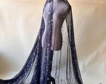 Puede incluir: Tela azul marino oscuro con un patrón celestial de estrellas y constelaciones. El material transparente está drapeado sobre un maniquí, mostrando su calidad fluida. La tela es ideal para crear prendas u objetos decorativos únicos.