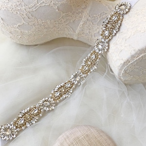 May include: A delicate bridal sash with a beaded design featuring clear and gold crystals. The sash is made of a soft, flexible material and is perfect for adding a touch of sparkle to any wedding dress.