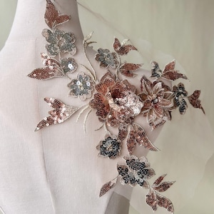 Può includere: Un'applicazione floreale delicata con un design di paillettes marroni e argento. L'applicazione presenta un gruppo di fiori e foglie, perfetto per aggiungere un tocco di eleganza a vestiti o artigianato.