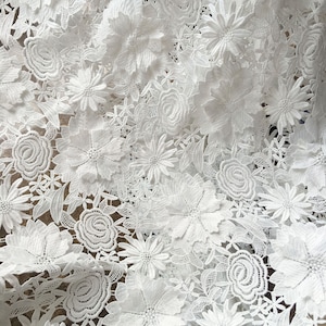 Pu&ograve; includere: Tessuto di pizzo bianco con un motivo floreale. Il tessuto &egrave; realizzato in pizzo delicato e intricato con un motivo floreale in rilievo.